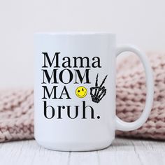 a white coffee mug with the words mama, ma and bruh on it next to a pink blanket