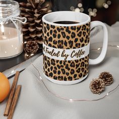 a leopard print coffee mug sitting on top of a table next to pine cones and candles