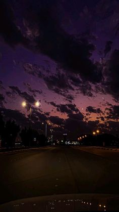 the night sky is lit up with street lights and clouds in the distance as seen from an empty parking lot