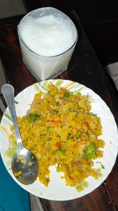 rice and vegetables on a plate next to a glass of milk with a spoon in it