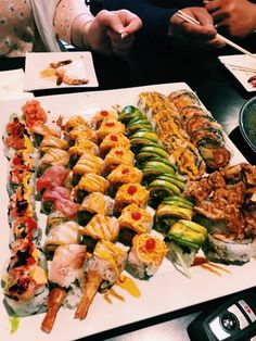 several different types of sushi on a white platter with chopsticks in front of them