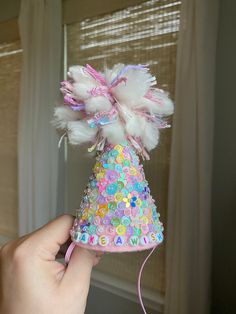 a hand holding a small party hat with sequins and feathers