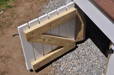 a wooden bench sitting on top of gravel next to a white wall and window sill