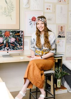 a woman sitting at a desk in front of a wall with pictures and flowers on it