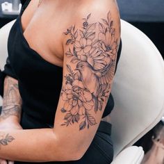 a woman sitting in a chair with her arm covered by flowers and a bird tattoo