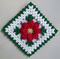 a crocheted square with a red flower on the center and green leaves in the middle