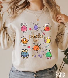 "This Pediatrics Department / PEDS Nurse Sweatshirt / Pediatrician Sweatshirt is so cute and perfect for working in Pediatrics! Makes a great gift for the PEDS Nurse or Pediatrician in your life! Makes a great gift or buy for yourself! See all of our Pediatric items here!: https://tinyurl.com/mpuwwyjb Say hello to your new favorite sweatshirt! It's a go-to classic lounge-able sweatshirt, that's also perfect for wearing out and about! Whether your day will consist of running errands, walking your Cute Long Sleeve Shirt With Funny Print, Cute Long Sleeve T-shirt For School, Pediatric Nursing Scrubs, Pediatrics Doctor, Pediatric Doctor, Peds Nurse, Nursing School Essential, Child Life Specialist, Nursing School Motivation