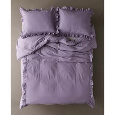 an unmade bed with purple sheets and pillows on top of it, next to a gray wall