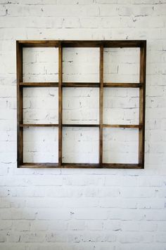 a white brick wall with an empty wooden shelf on the bottom and one window in the middle