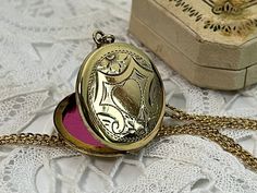 "Description: An antique etched round gold plated locket on a 14K gold filled chain. The front of this pendant features an etched central heart that is surrounded with ornate lines in a geometric type of design with angled sides around the remainder of the front. There are small etched flowers at the top and the bottom of the central heart shape. The back of this locket is plain with no design and has a shiny finish. The sides of the round locket are somewhat flat, not rounded as most lockets ar Gold Heirloom Brass Locket Necklace, Heirloom Gold Brass Locket Necklace, Victorian Etched Locket Necklace Gift, Victorian Etched Locket Necklace As Gift, Victorian Etched Locket Necklace For Gift, Gold Necklace With Antique Finish For Keepsake, Victorian Gold Locket Necklace With Vintage Charm, Ornate Gold Brass Locket Necklace, Ornate Gold Locket Necklace In Brass