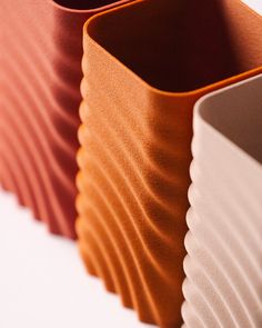 three different colored vases sitting side by side on a white surface, one is orange and the other is brown