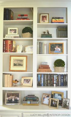 a white bookcase filled with lots of books and framed pictures on top of it