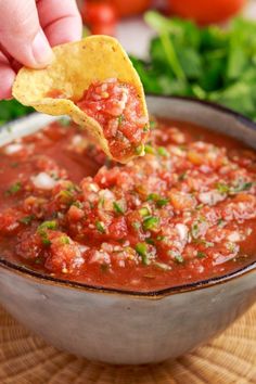 a hand dipping a tortilla chip into a bowl of salsa