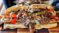 a sandwich with meat, peppers and onions on a cutting board next to a knife