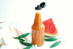 a bottle filled with liquid next to slices of watermelon and green beans on a white surface