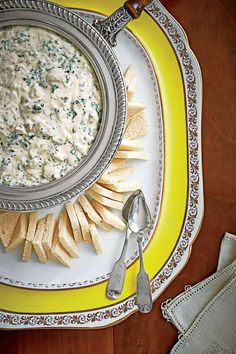 a bowl of dip with crackers on a yellow and white plate next to it