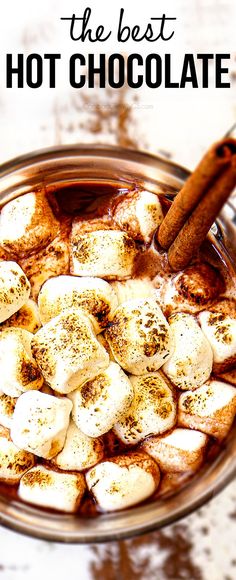 hot chocolate with cinnamon sticks and marshmallows in a glass bowl on a table