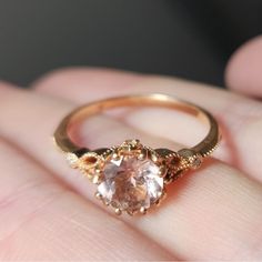 a close up of a person's hand holding a ring with an orange and white diamond