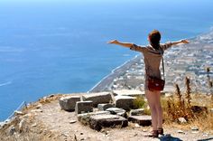 a woman standing on top of a hill with her arms outstretched