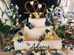 a wedding cake sitting on top of a table with blue and white flowers around it