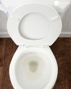 a white toilet bowl with the lid up on a wooden floor in a bathroom stall