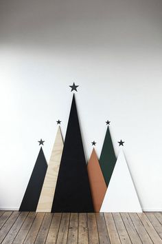 three wooden christmas trees with black and white stars on the top, against a white wall