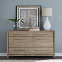 a white vase sitting on top of a wooden dresser next to a framed photograph and lamp