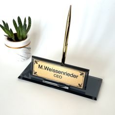 a pen is sitting on top of a desk next to a potted plant and a plaque