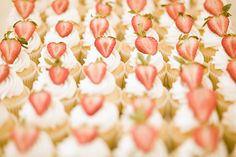 cupcakes with white frosting and strawberries on them are arranged in rows