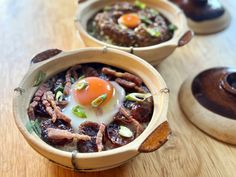 two wooden bowls filled with meat and an egg on top of each bowl, sitting on a table