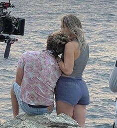 two women hug each other as they stand on rocks near the water and take pictures