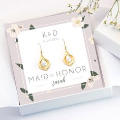 a pair of gold earrings sitting on top of a white box next to some flowers