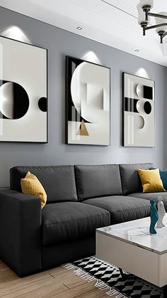 a modern living room with grey couches and yellow pillows on the coffee table in front of three abstract paintings