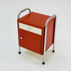 a small red and white cabinet sitting on top of a white floor next to a metal hand rail