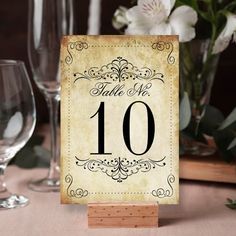 a table number sign sitting on top of a wooden stand next to wine glasses and flowers