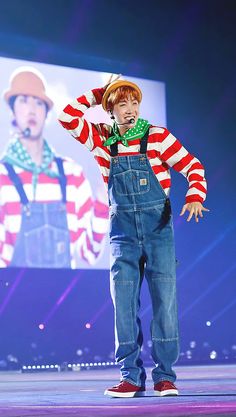 a boy in overalls and a hat on stage with his hands behind his head