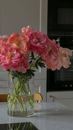 pink flowers are in a clear vase on the kitchen countertop, with an oven in the background