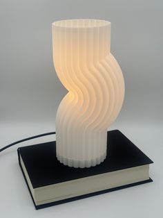 a white lamp sitting on top of a book next to a light that is shaped like a spiral