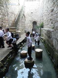 several children in school uniforms are standing on stepping stones and looking at the water that is running through them