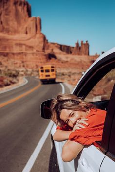 a woman leaning out the window of a car on a road with mountains in the background