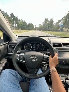 a person driving a car on the road with their hands on the steering wheel,