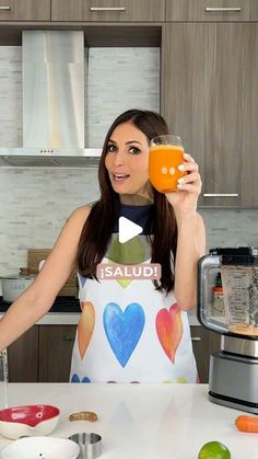 a woman is holding up a glass of orange juice in her hand while standing at the kitchen counter