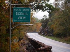 a road sign that is on the side of a hill next to some trees and bushes