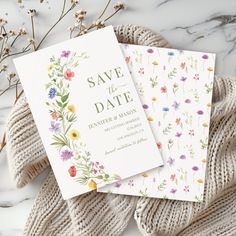 two floral save the dates cards on top of a white marble table with dried flowers