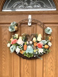 a wreath with flowers and a stuffed animal hanging on the front door to welcome guests