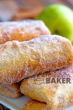 some sugar coated doughnuts on a plate with an apple in the background