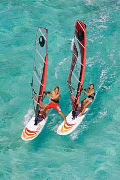 two people riding windsurfers in the ocean on clear blue water with bright colors