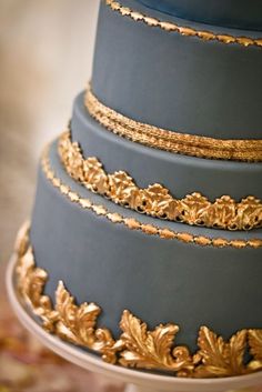 a three tiered cake with gold leaf decorations on the top and bottom layer is dark blue