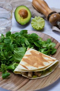 a tortilla on a plate with spinach and avocado next to it