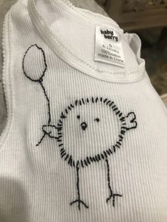 a white shirt with a drawing of a bird holding a balloon on it's chest